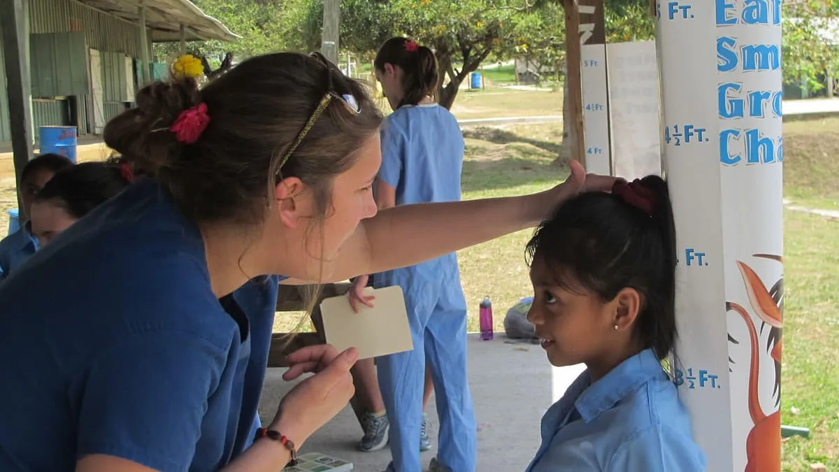 Student measuring a child's height at a community clinic